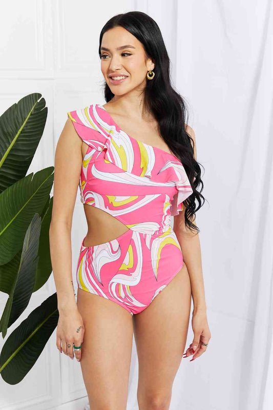 Marina West Swim Vitamin C Asymmetric Cutout Ruffle Swimsuit in PinkBold and printed with a retro design, this cutout swimsuit is fabulously fun! Featuring an asymmetrical neckline and a ruffle trim, this swimsuit is sure to put the Marina West Swim VitaminMarina West Swim Vitamin