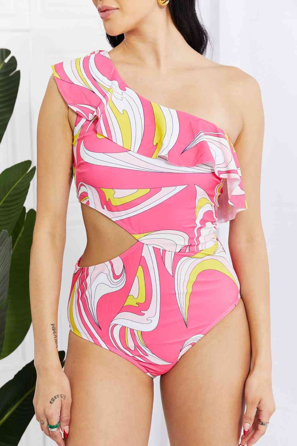 Marina West Swim Vitamin C Asymmetric Cutout Ruffle Swimsuit in PinkBold and printed with a retro design, this cutout swimsuit is fabulously fun! Featuring an asymmetrical neckline and a ruffle trim, this swimsuit is sure to put the Marina West Swim VitaminMarina West Swim Vitamin