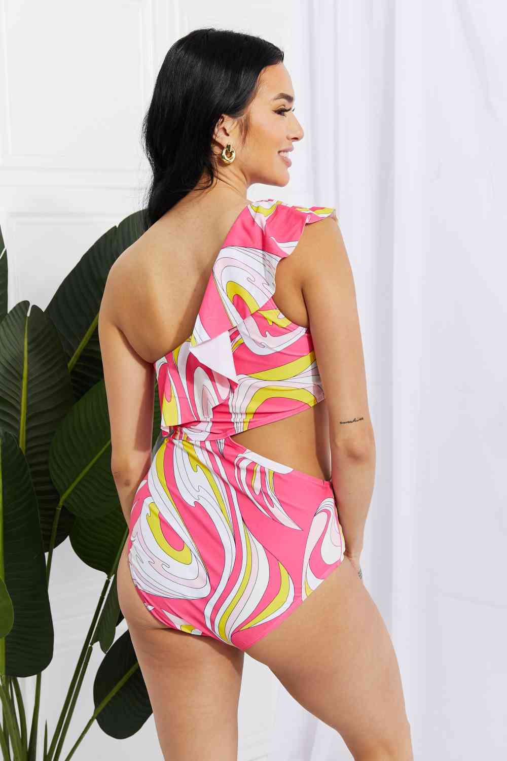 Marina West Swim Vitamin C Asymmetric Cutout Ruffle Swimsuit in PinkBold and printed with a retro design, this cutout swimsuit is fabulously fun! Featuring an asymmetrical neckline and a ruffle trim, this swimsuit is sure to put the Marina West Swim VitaminMarina West Swim Vitamin